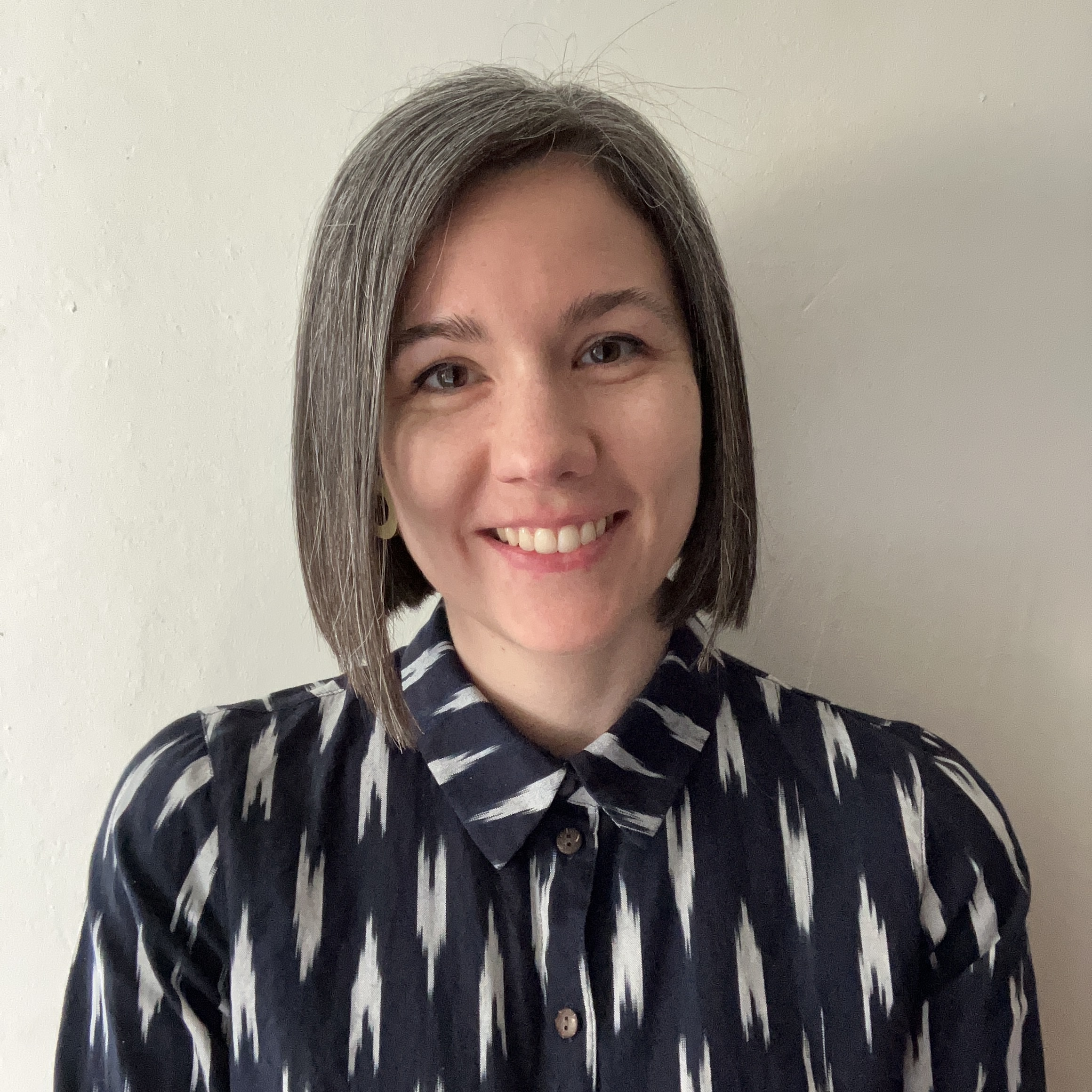 Alex is a smiling white woman in her thirties, wearing a patterned dress.